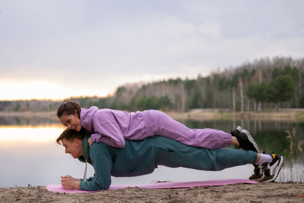 Couple-exercising-together-outdoors-man-doing-plank-with-woman-on-his-back