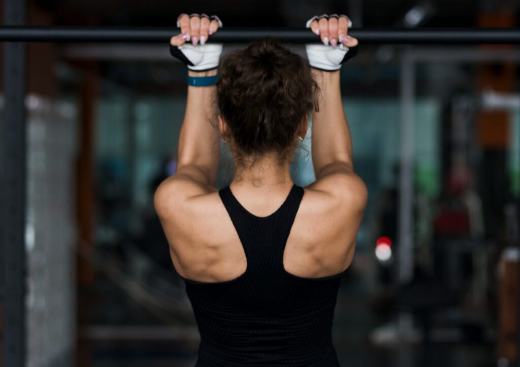 Woman-performing-chin-up-exercise-in-gym-back-view