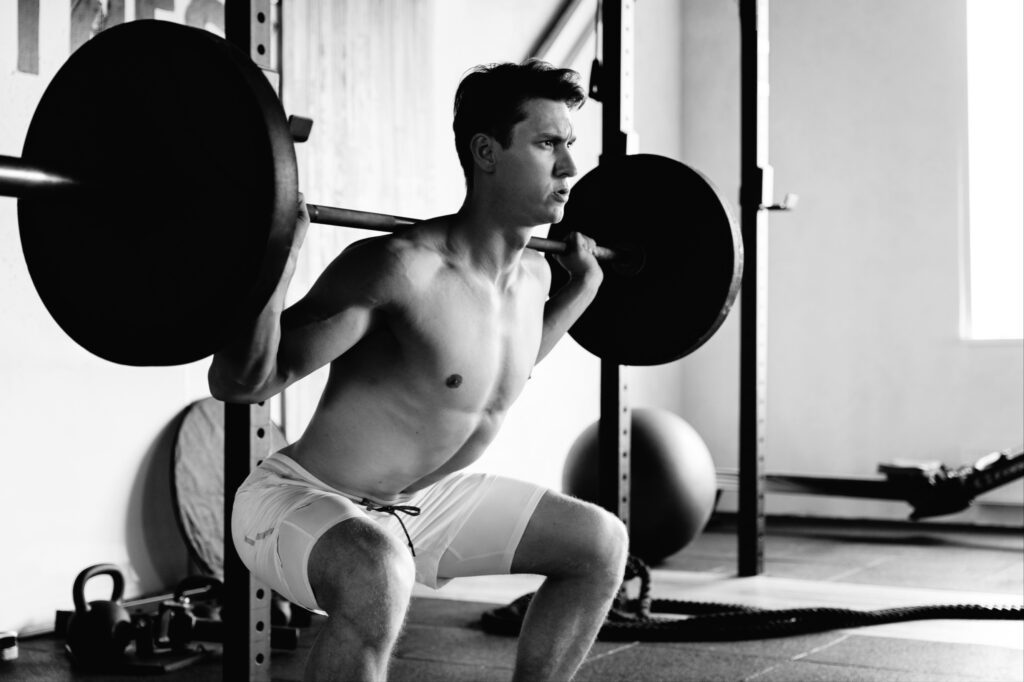 Man-performing-barbell-back-squats-in-gym