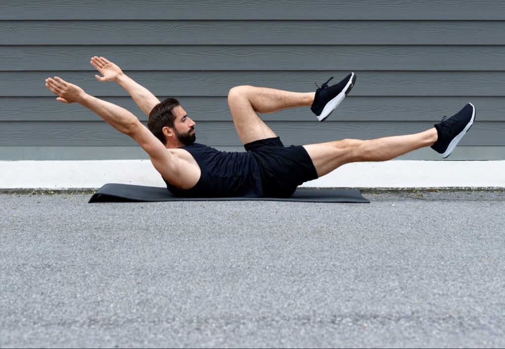 Man-doing-advanced-hollow-body-hold-variation-on-exercise-mat-outdoors