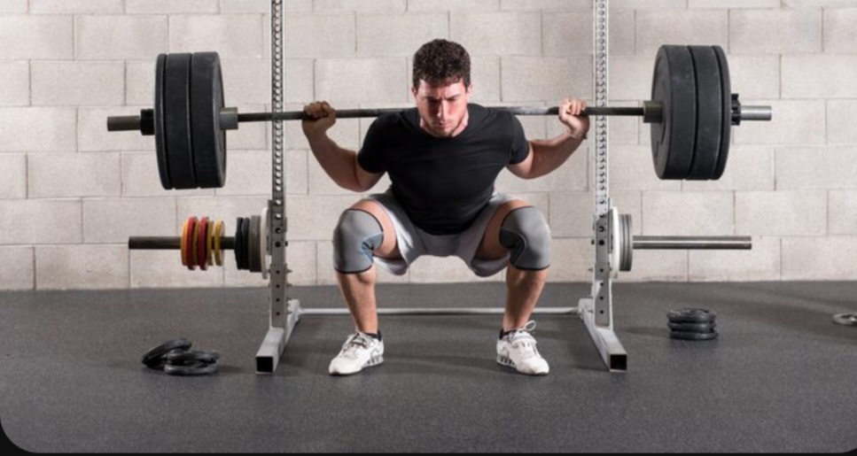 Man-doing-heavy-squat-with-barbell-on-squat-stand-in-gym