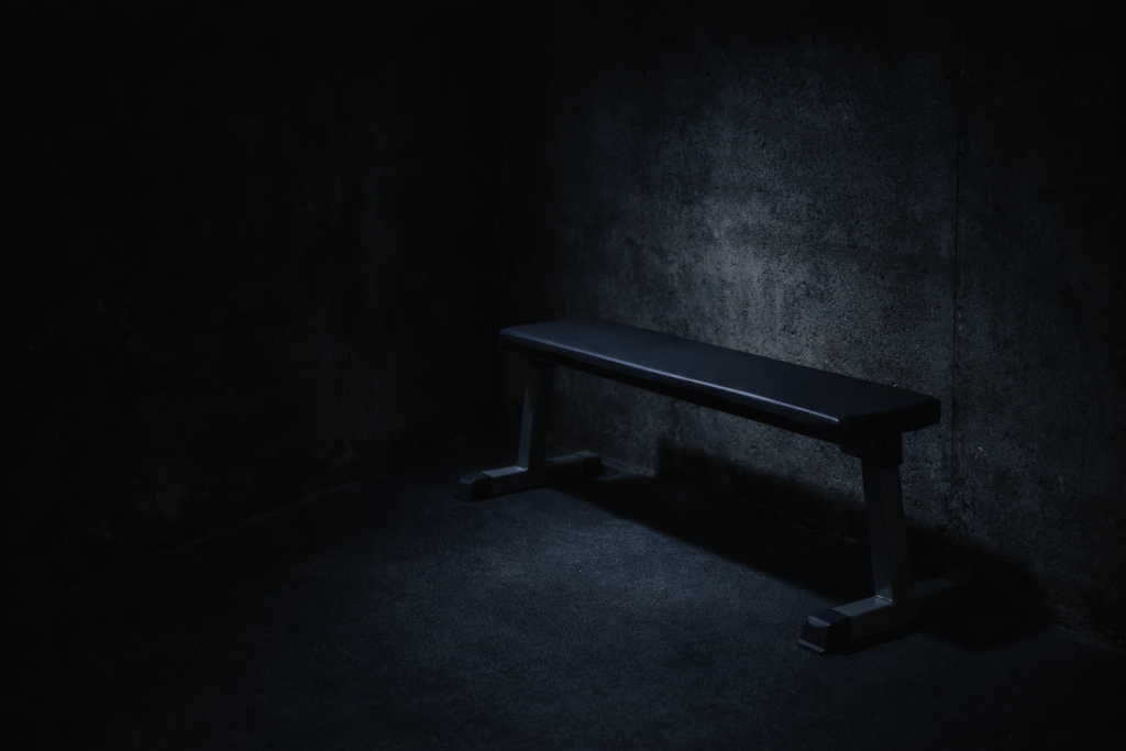 Low-weight-bench-positioned-in-dark-gym-corner